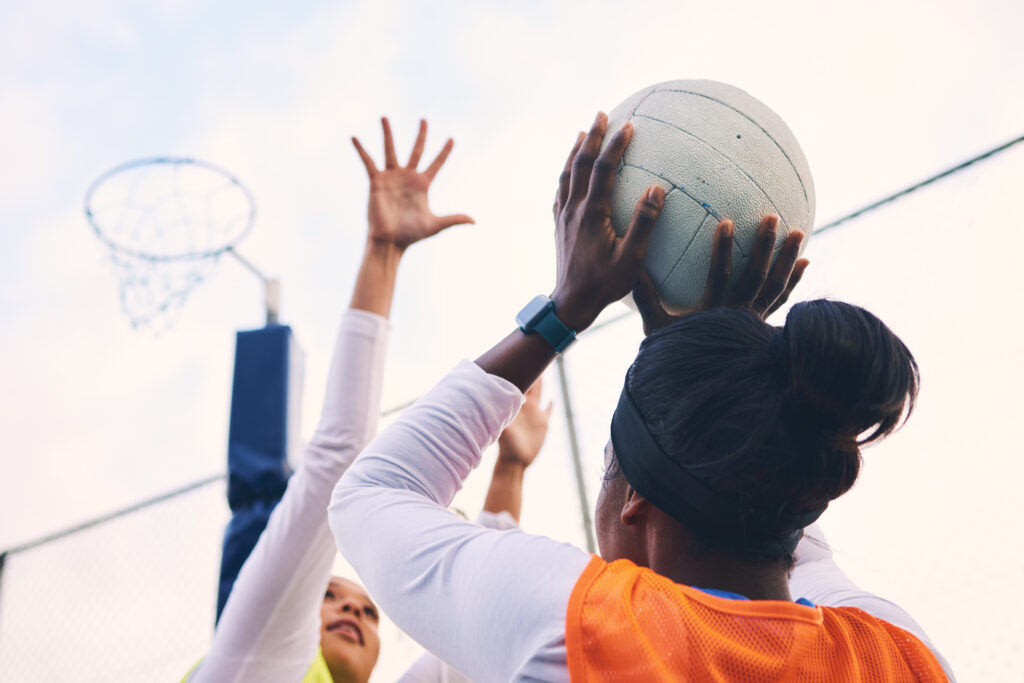 Netball, goal shooter and fitness of a girl athlete group on an outdoor sports court. Aim, sport ga.