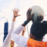 Netball, goal shooter and fitness of a girl athlete group on an outdoor sports court. Aim, sport ga.