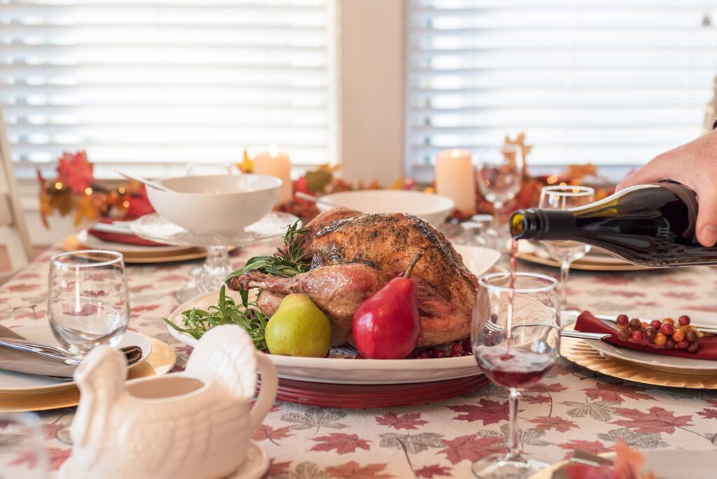 Holiday dinner table with roasted turkey, man pouring red wine in the foreground