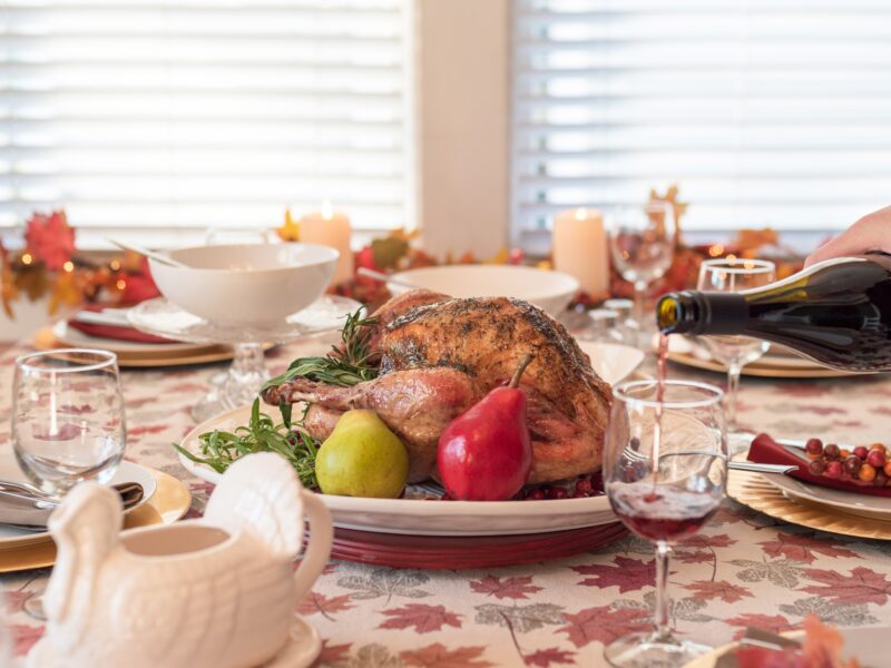 Holiday dinner table with roasted turkey, man pouring red wine in the foreground